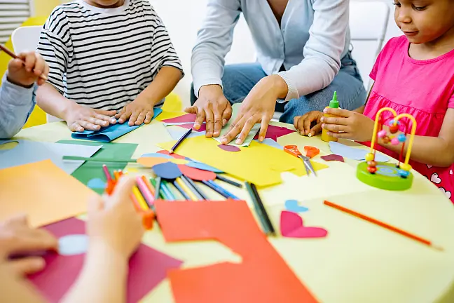 Eine Gruppe Kinder, die mit einer pädagogischen Fachkraft basteln